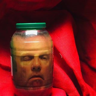 a glass jar with a man's face in it on top of a red cloth