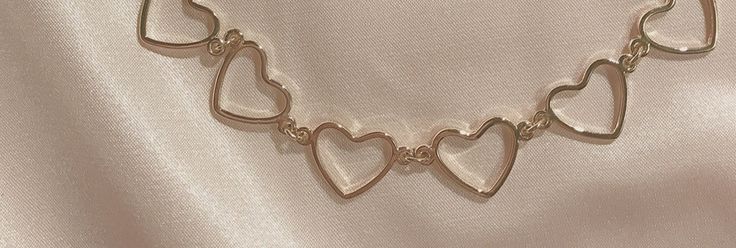 a gold necklace with hearts on it is laying on a satin surface, in the shape of an open heart