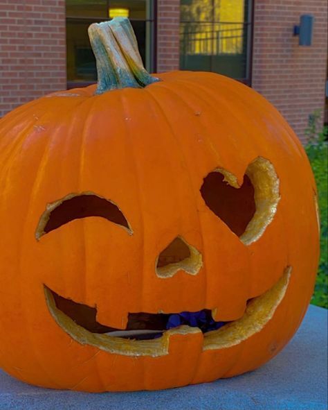 a carved pumpkin sitting on top of a cement slab in front of a brick building