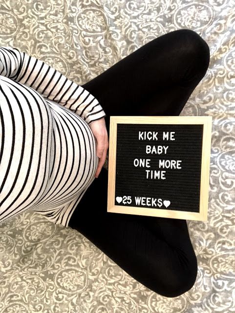 a woman is holding a sign that says kick me baby one more time 5 weeks