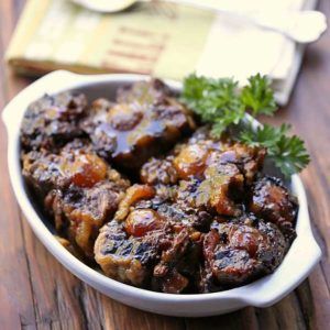 a white bowl filled with meat on top of a wooden table next to a napkin