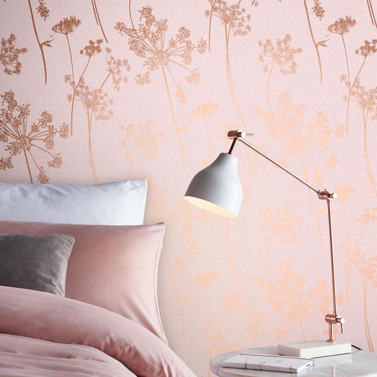 a bedroom with pink and gold wallpaper, bedding and a lamp on the side table