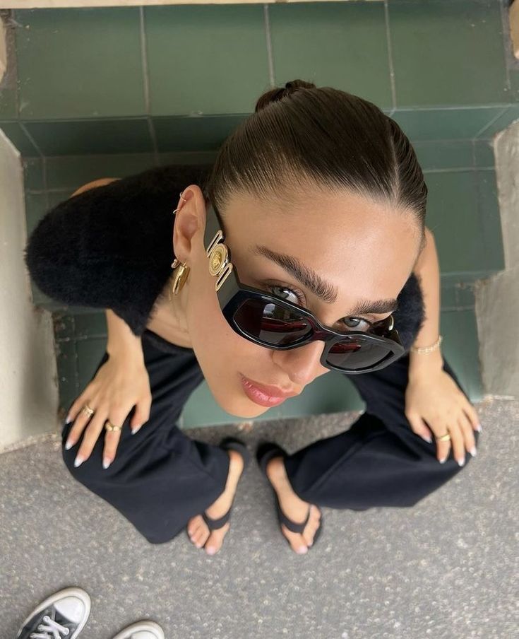 a woman wearing sunglasses looking down at the ground with her hands on her hips and feet up