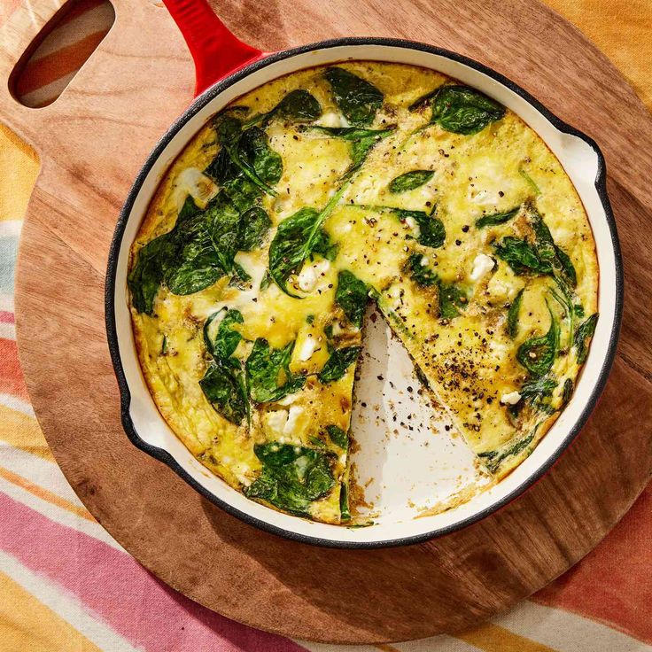 an omelet with spinach and cheese in a pan on a wooden platter