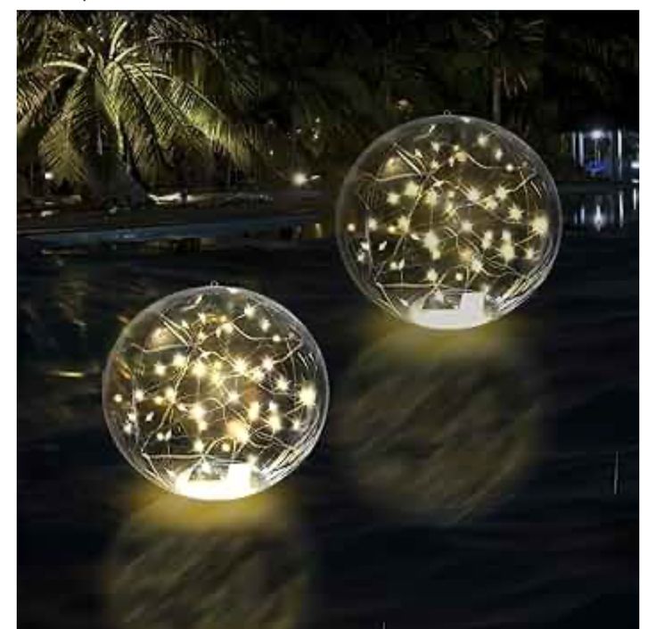 two glass balls with lights on them sitting in the middle of a body of water