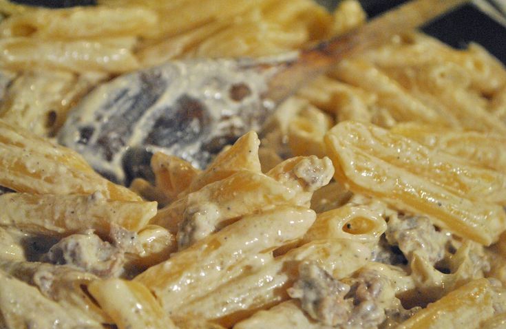 pasta with meat and cheese is being cooked in a skillet on the stove top