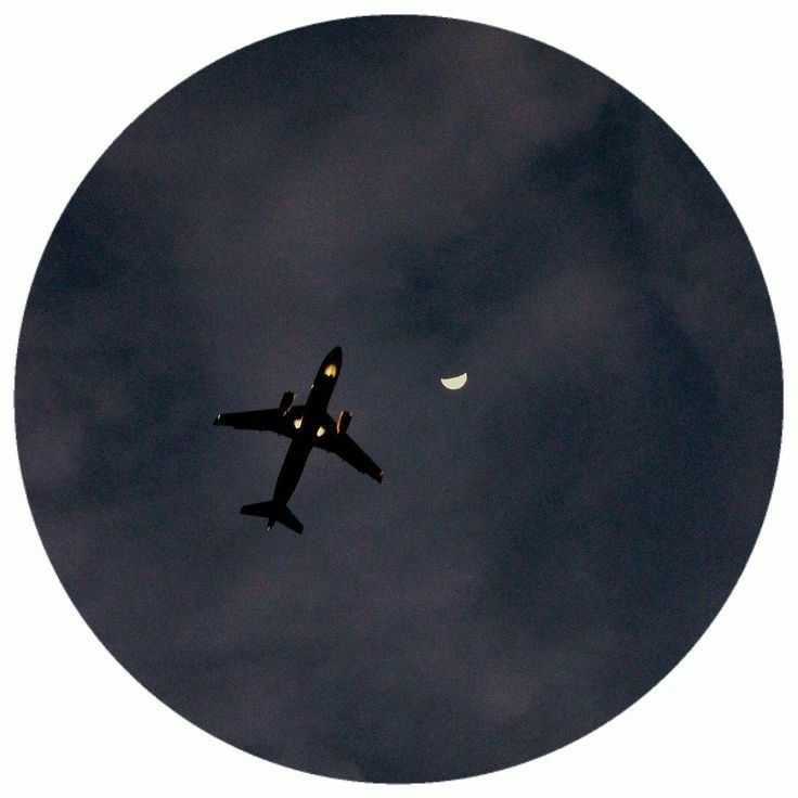 an airplane is flying in the sky with a half moon behind it and dark clouds