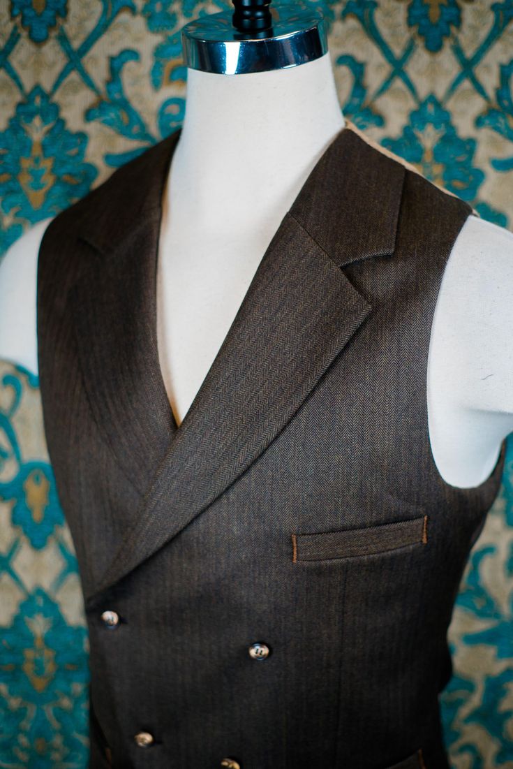 "ABOUT THIS STYLE: The style features a 1930s style jacket with a low gorge and a ticket pocket, a double-breasted notch collar vest, and a high-waisted pant with an extended waistband tab. With all of our designs, we look backward across the great history of menswear and try to bring forward is best and most fresh from the past, discarding what does not speak to our present age, but retaining all of the traditional craftsmanship and quaility. The suit is made from a vintage style herringbone su Fitted Double-breasted Three-piece Suit With Single Button, Three-piece Suit With Notch Lapel For Tailoring, Elegant Brown Vest With Notch Lapel, Elegant Brown Notch Lapel Vest, Classic Vest With Lapel Collar For Fall, Semi-formal Single-breasted Vest With Lapel Collar, Fitted Double Breasted Suit With Notch Lapel, Fitted Vest With Buttons And Lapel Collar, Classic Fitted Double-breasted Three-piece Suit