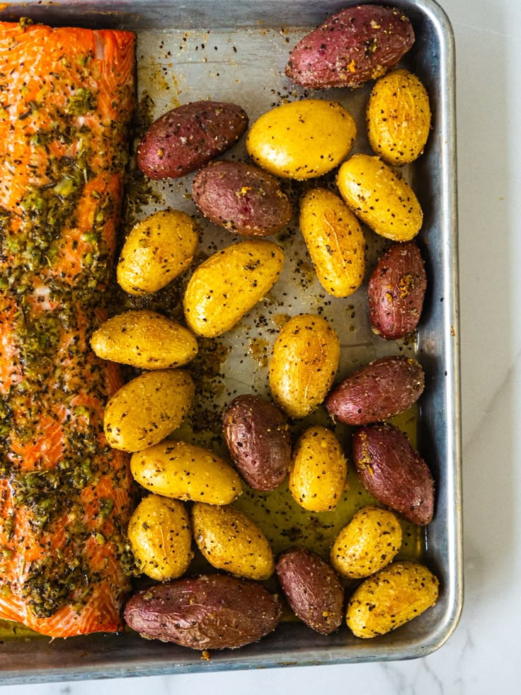 baked salmon and potatoes in a pan on a counter top with seasoning sprinkles