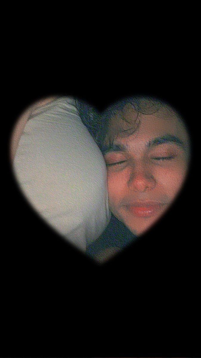 a man is laying in bed with his eyes closed and the heart shaped pillow behind him