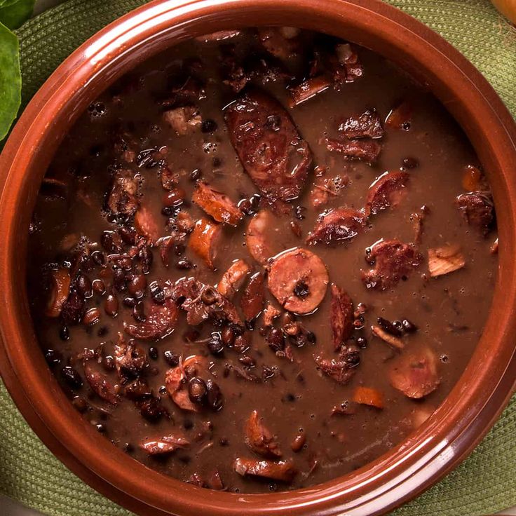 a close up of a bowl of soup on a table with vegetables and meats