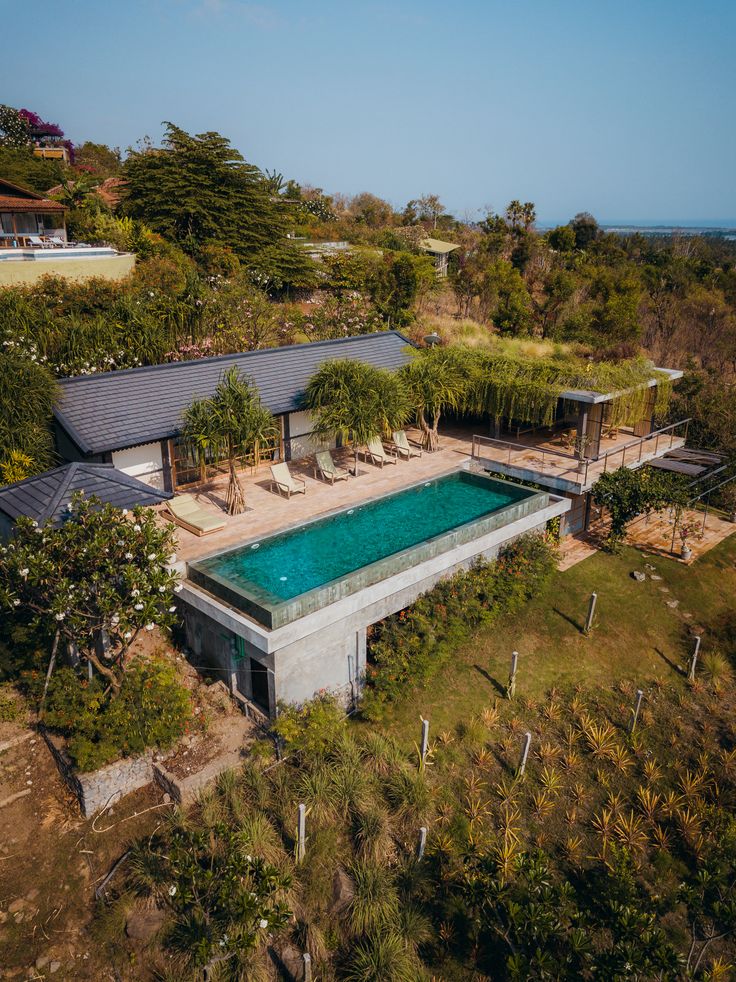 an aerial view of a house with a swimming pool in the foreground and trees surrounding it