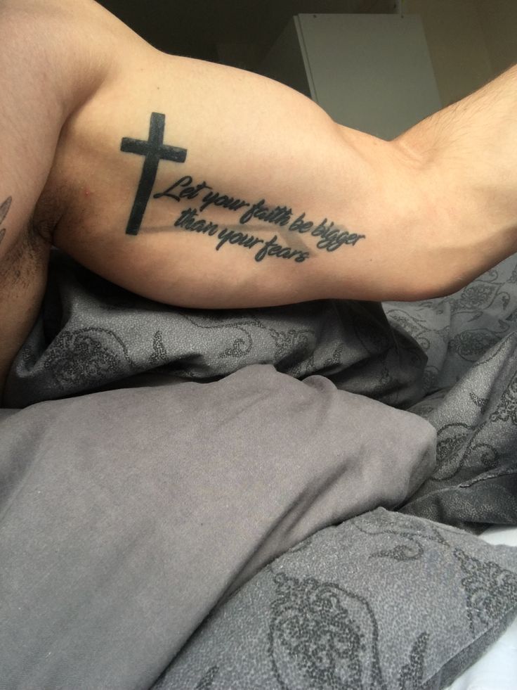 a man laying on top of a bed with a cross tattoo on his arm and chest