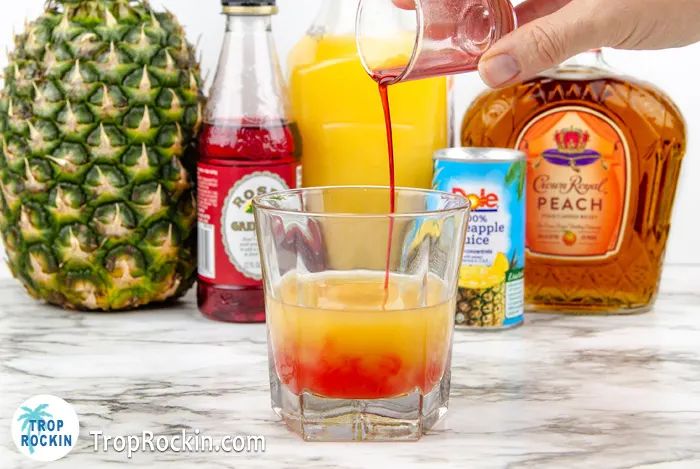 someone pouring orange juice into a glass with pineapples and other drinks in the background