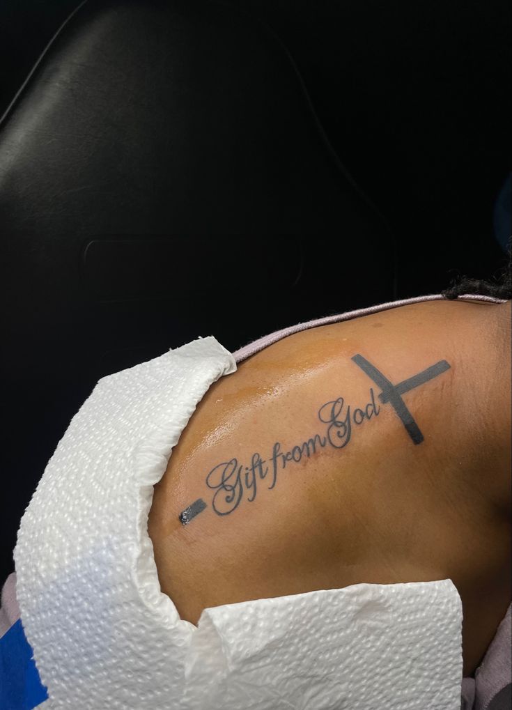 a woman with a cross tattoo on her arm and the words gift from god written in cursive font