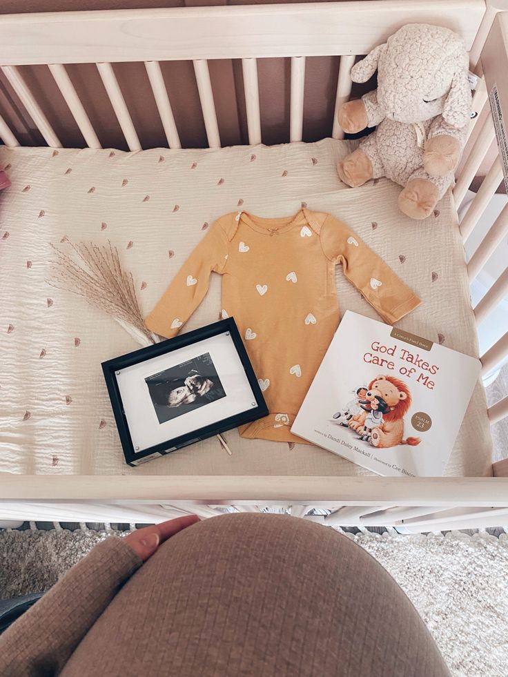 a baby in a crib next to a book and teddy bear on the floor