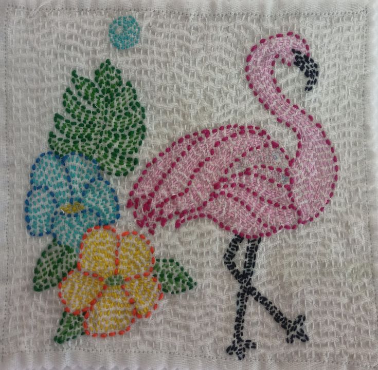 a pink flamingo standing next to flowers on a piece of white fabric with green leaves