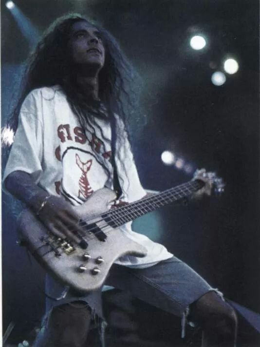 a man with long hair and dreadlocks playing a bass guitar on stage at a concert