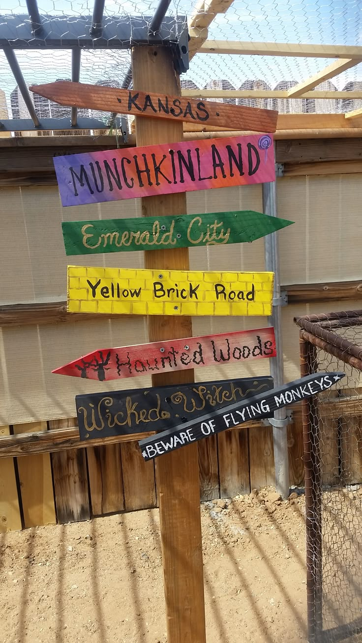 a wooden sign with many different colored signs attached to it's sides in front of a fence