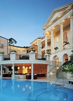 an outdoor swimming pool in front of a large white building with columns and balconies