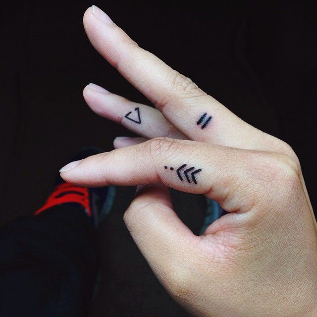 two fingers with small tattoos on them, one has an arrow and the other has a heart