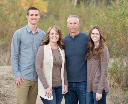 three adults and one child posing for a family photo in front of some trees with yellow leaves