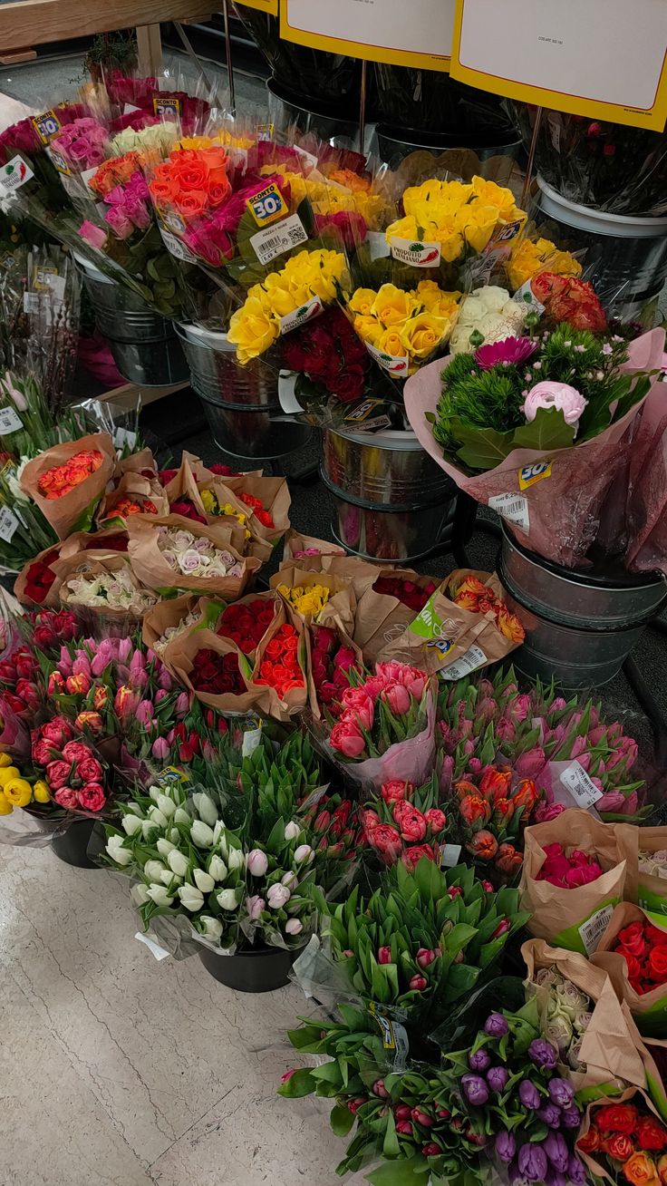 many different types of flowers in buckets on the ground with price signs behind them