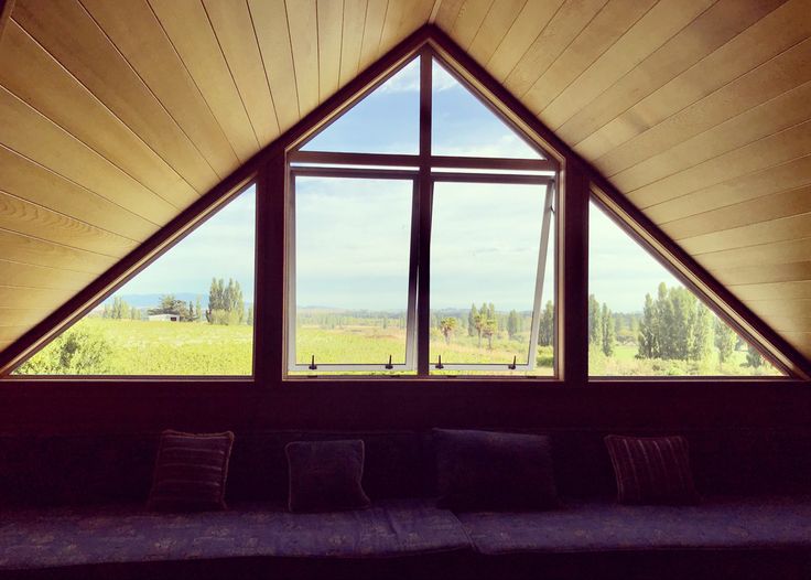 a couch sitting in front of a large window on top of a wooden wall next to a green field