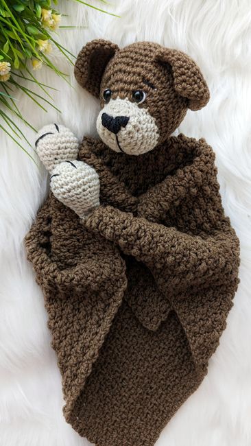 a crocheted teddy bear wrapped in a blanket on top of a white rug