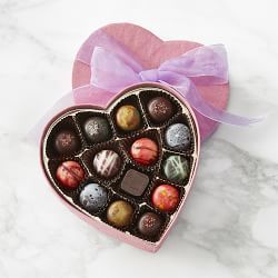 a heart shaped box filled with chocolates on top of a marble countertop next to a pink bow