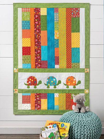 a stuffed animal sitting on top of a pillow next to a quilted wall hanging