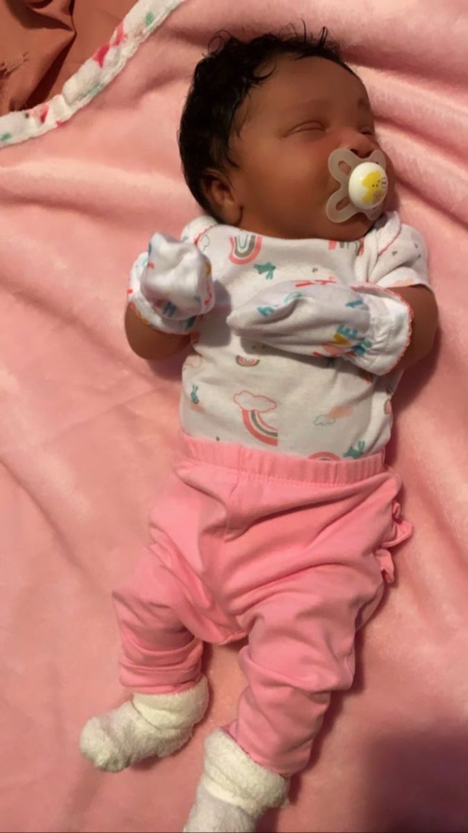 a baby laying on top of a pink blanket with pacifier in it's mouth