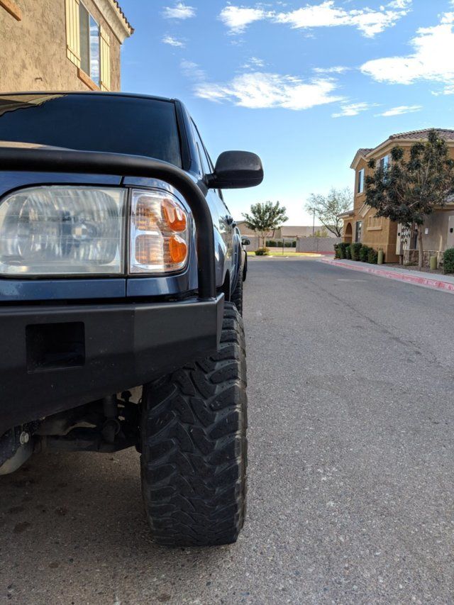 the front end of a black truck parked on the side of a road next to houses