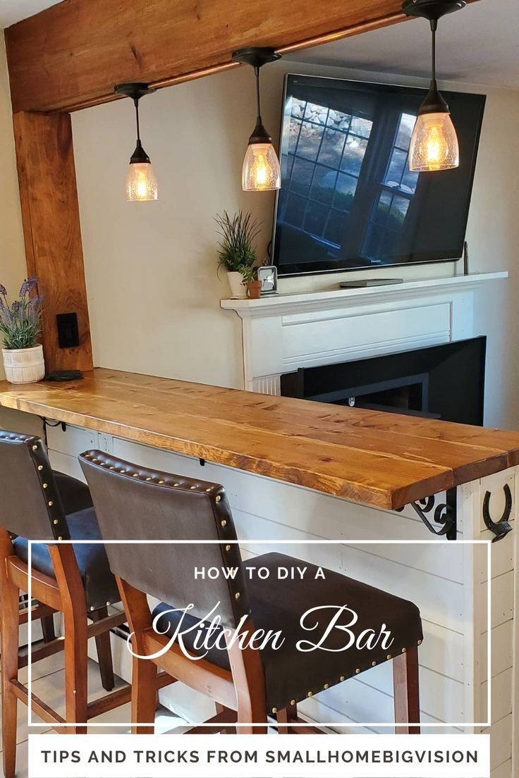 a kitchen bar with three chairs and a television mounted on the wall above it, in front of a fireplace