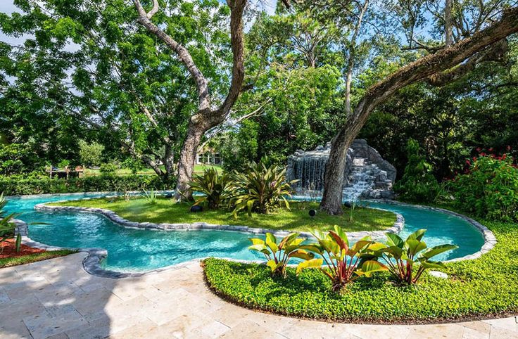 an outdoor swimming pool surrounded by lush green trees and shrubs, with a waterfall in the middle