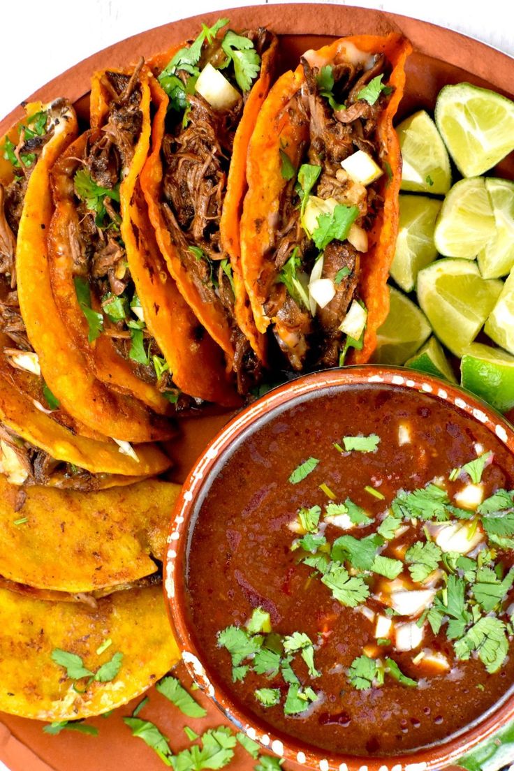 mexican food with tortillas, salsa and limes on a plate next to sliced avocado