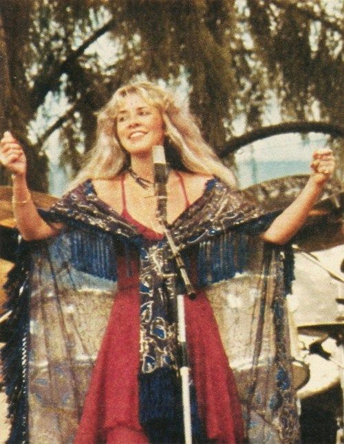 a woman standing in front of a microphone with her hands up and wearing a red dress