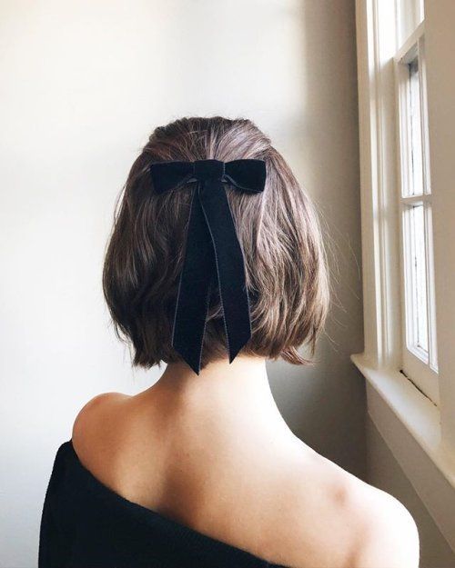 the back of a woman's head with a black bow in her hair, standing next to a window