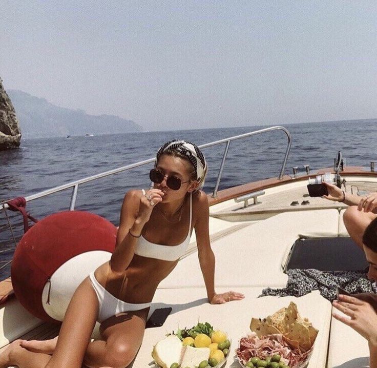 two women sitting on a boat eating food and drinking wine while another woman looks at the camera