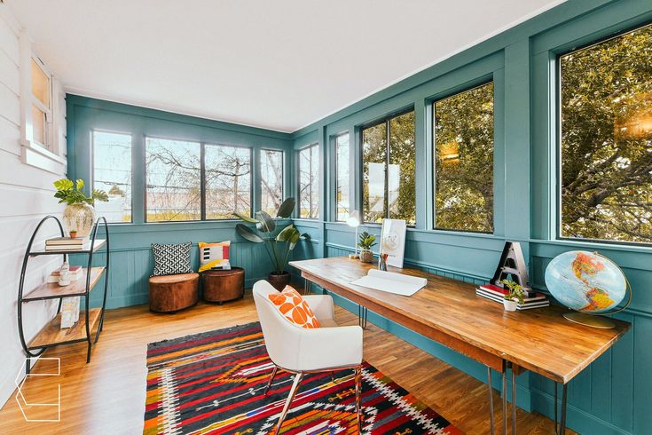 a room with blue walls and wooden floors has a desk, chair, and large windows