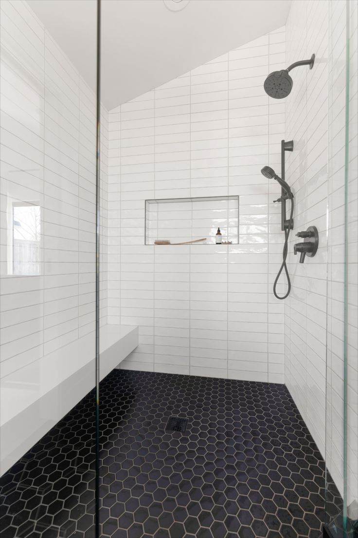 a bathroom with black and white hexagonal tiles on the floor, shower head, and glass walls