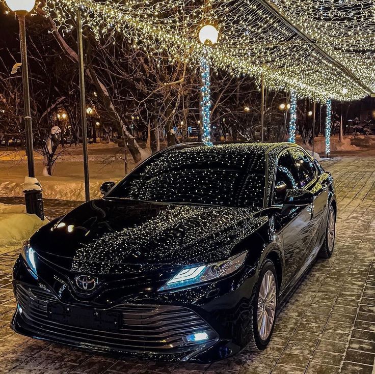 a black car is parked on the street in front of some christmas lights and trees