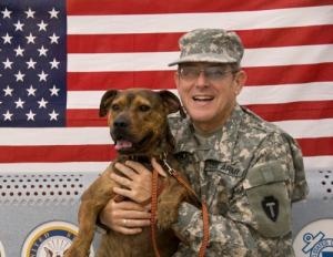 a man in uniform holding a dog with an american flag on the wall behind him