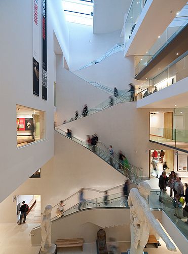 many people are walking up and down the escalator in a building with glass balconies