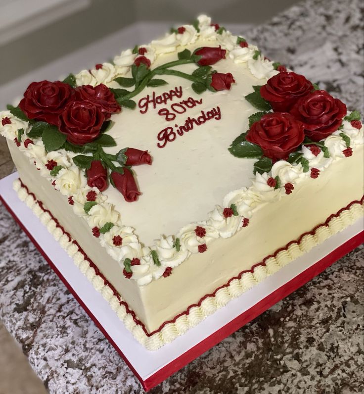 a heart shaped birthday cake with red roses on the top and white frosting, sitting on a granite countertop