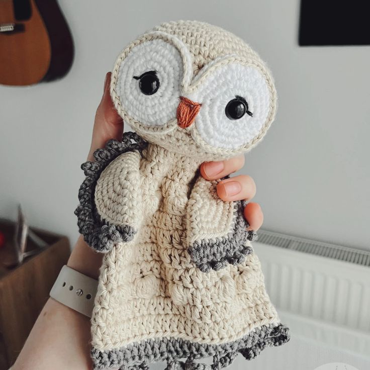 a person holding up a crocheted owl doll with big eyes and a scarf