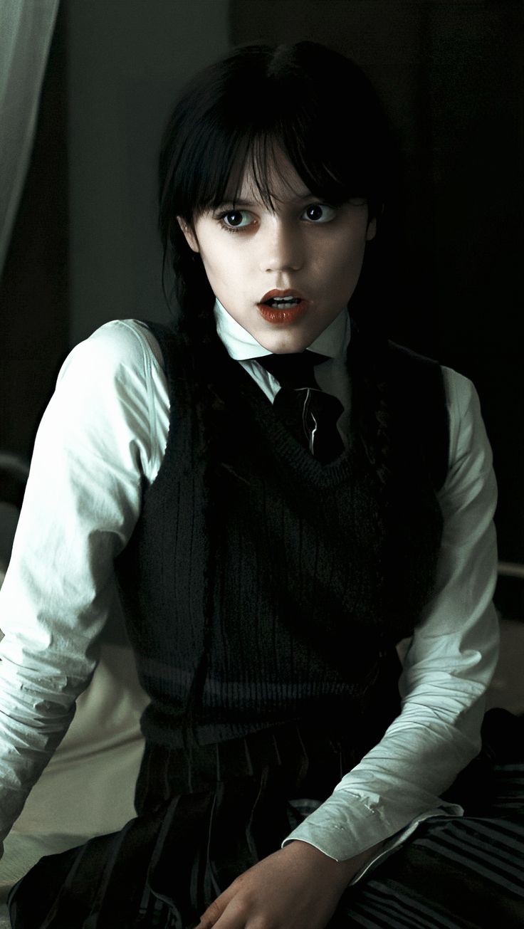 a woman with black hair sitting on a bed wearing a white shirt and black tie