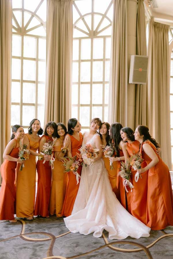 a group of women standing next to each other in front of a window holding bouquets