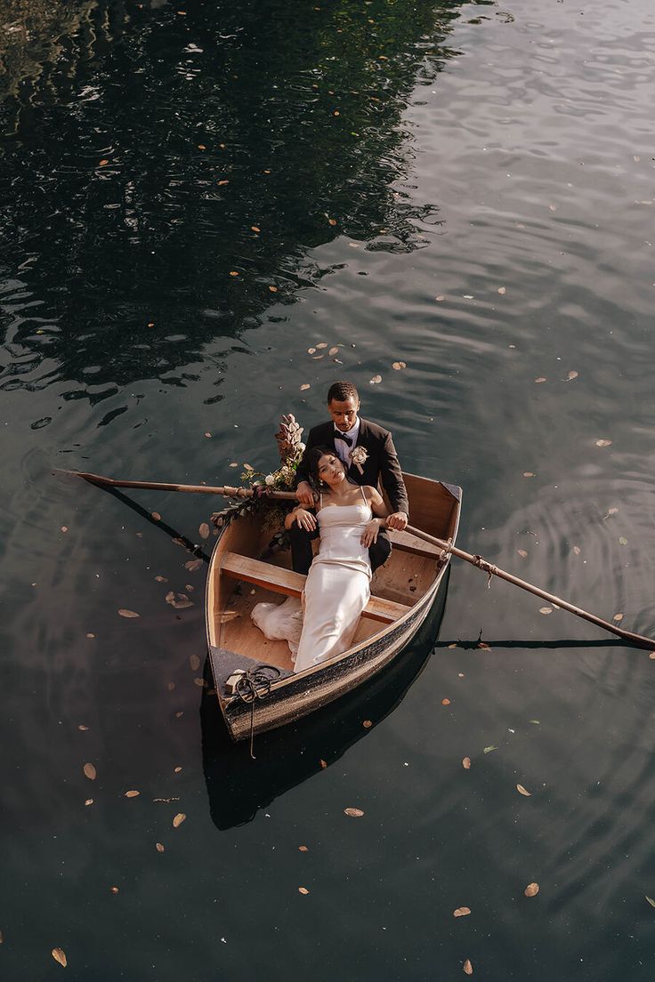 a bride and groom in a row boat on the water with leaves floating around them