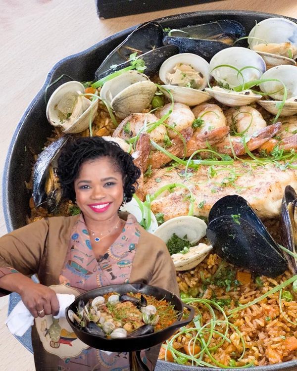 a woman standing in front of a large pan filled with seafood and clambers